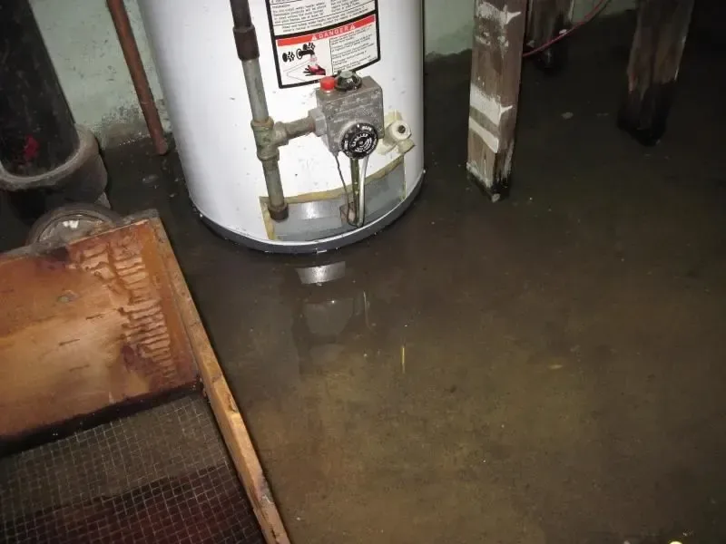 A leaking water heater standing in a puddle on a utility room floor